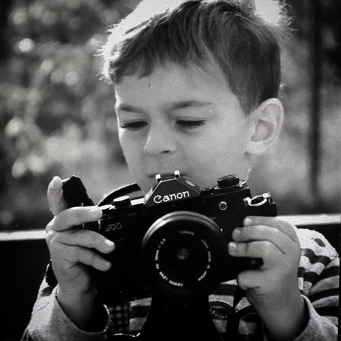 Young Mike Mala age 5 holding a Canon A-1 35mm film camera — a lifelong passion for photography